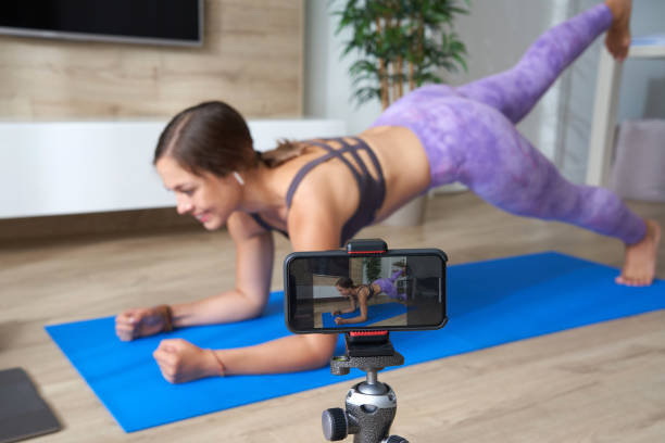 jeune blogueuse enregistrant une vidéo sportive à la maison en faisant du yoga dans un salon avec un ordinateur portable - video home video camera shooting video still photos et images de collection