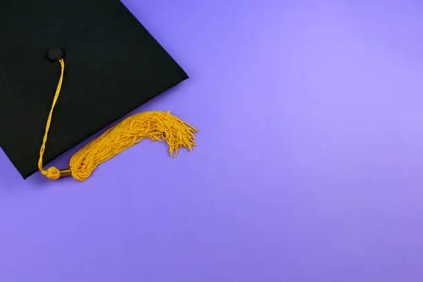 Photo of Back to school. Black graduation cap on a purple background. Graduation concept. Black Mortar Board Cap