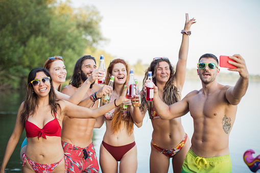 Group of friends dancing at party on deck. They are happy and joyful. Wearing swimsuits and making selfie.