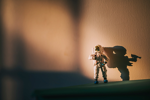 toy astronaut standing against wall with harsh shadow