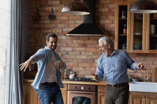 Excited grownup son and senior dad having fun in kitchen Excited grownup son and happy senior dad having fun in kitchen, dancing to music, singing, laughing, exercising, enjoying activity together. Intergenerational family friendship concept old person listening to radio stock pictures, royalty-free photos & images