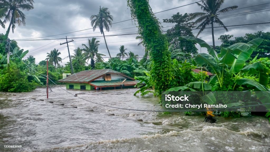 A rural home being submerged by floodwaters caused by torrential rain in the Philippines. Rising water levels submerging a house as heavy monsoon rains cause major floods in Baco, Oriental Mindoro, Philippines on July 23, 2021. Flood Stock Photo