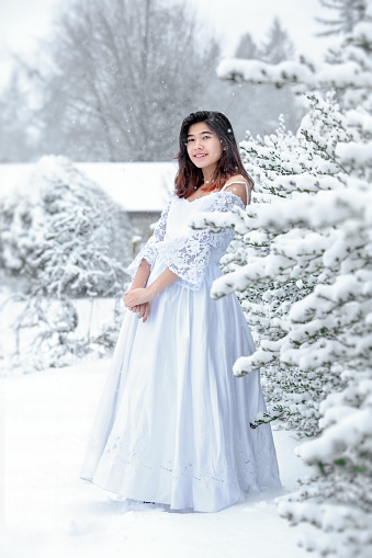Biracial teen girl wearing lace white dress standing outside in snow during winter