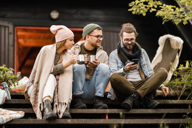 amigos felices usando el teléfono móvil en un patio frente a una casa de campo. - telephone cabin fotografías e imágenes de stock