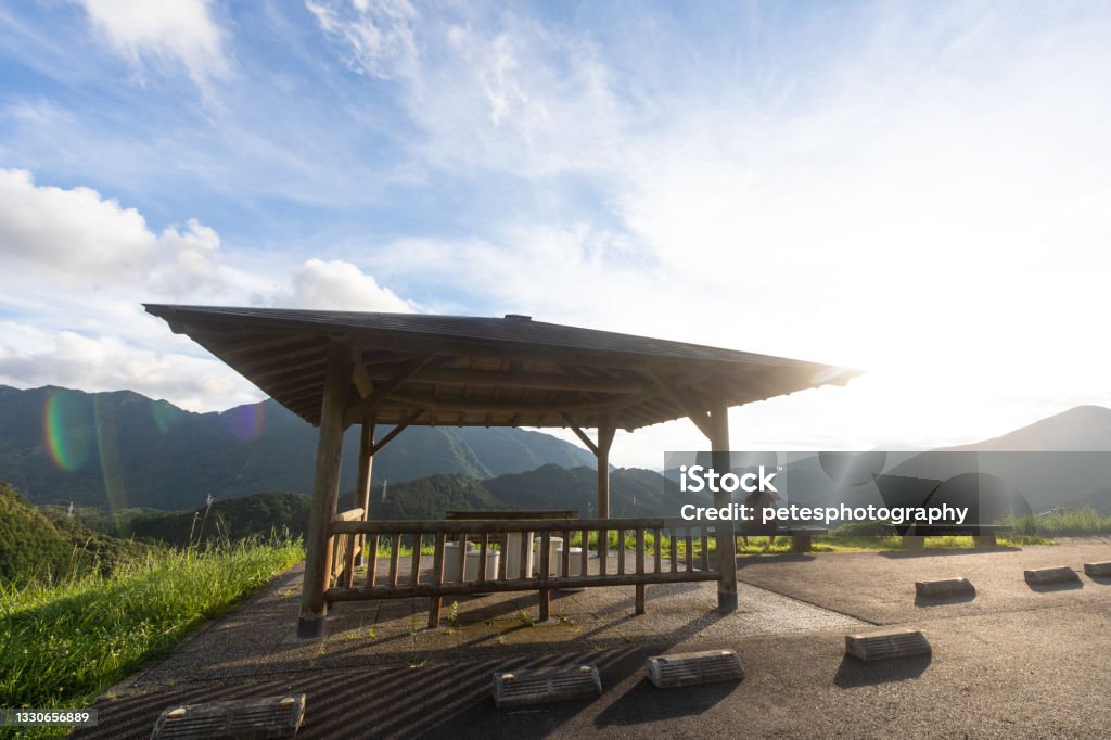 One person enjoying view over rice field terrace of Kumano, Mie The famous mountain rice field terraces in Kumano area of Mie Prefecture. A woman sits on a bench enjoying the late afternoon view of the fields and surrounding mountains by a car park rest area. Rest Area Stock Photo