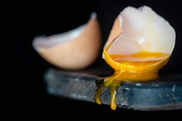 istock Broken egg shell with dripping yolk on wooden cutting board on black background, close up 1330657796