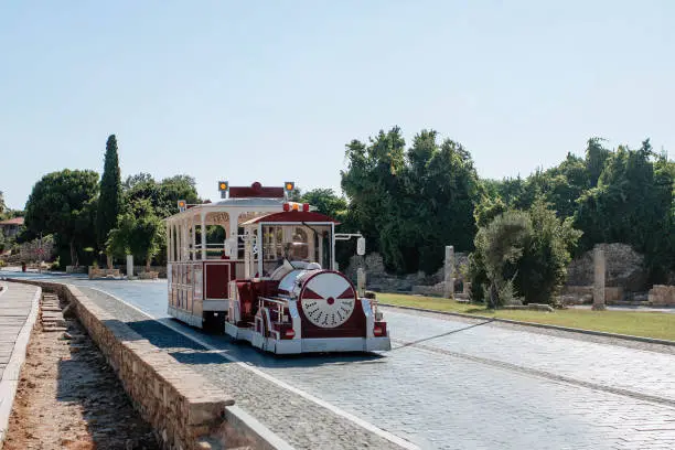 Photo of A red tourist tram rides along the cobblestone road of the city of Side in Turkey. Discernment for vacationers and transportation of tourists to the sights of the city