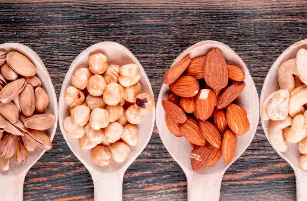 Assorted nuts and dried fruits in a wooden spoons with pecan, pistachios, almond, peanut, cashew, pine nuts top view on a wooden background free space for your text