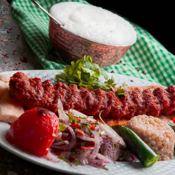 From above adana kebab with rice and fried vegetables and chopped onion and ayran in white plate on stone background