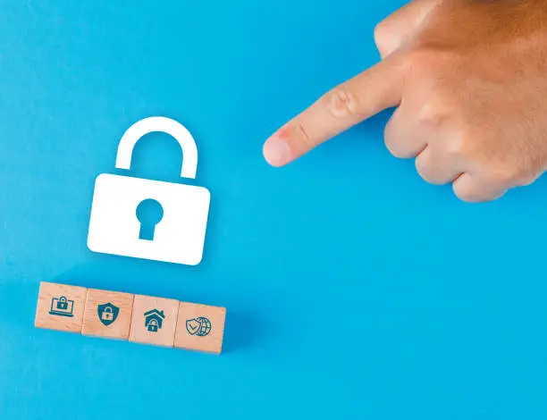 Security concept with wooden blocks, paper lock icon on blue background flat lay. man hand pointing. horizontal image