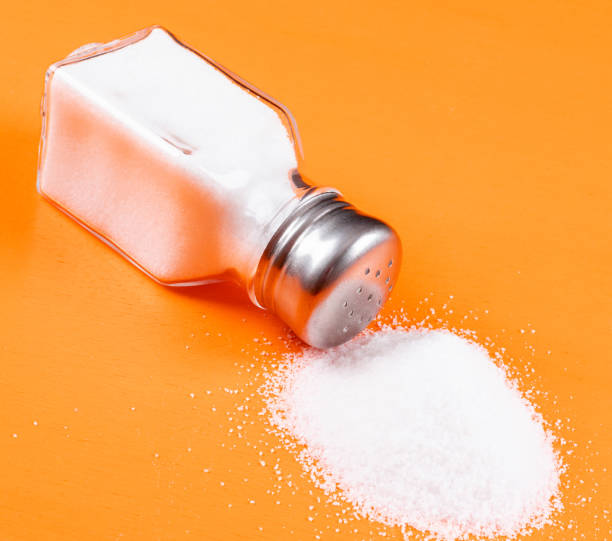 high angle view sea salt coming out of salt shaker on orange background. horizontal - saleiro de mesa imagens e fotografias de stock