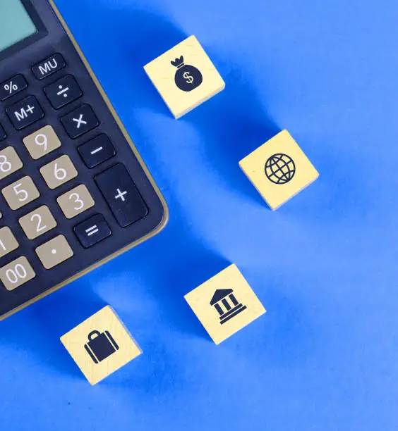 Financial concept with icons on wooden cubes, calculator on blue background flat lay.
