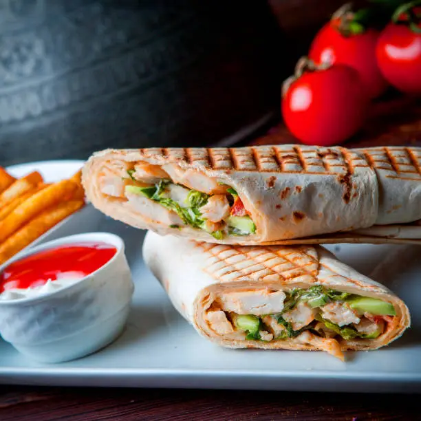 Side view shawarma pita roll with chicken and fried potatoes on a wooden background