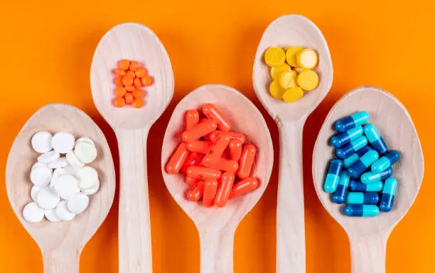 Top view colorful pills in wooden spoons on orange background