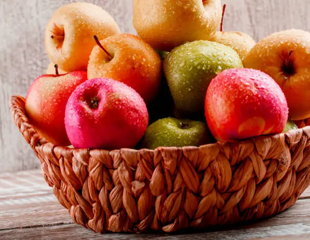 Apples with drops in a wicker basket on light wooden and grunge background. side view.