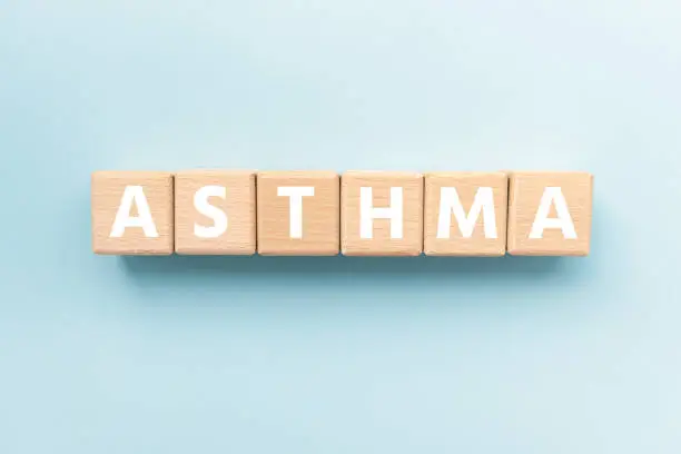 Photo of Text ASTHMA on wooden cubes on blue background. Long-term inflammatory disease of the airways of the lungs. Square wood blocks. Top view, flat lay.