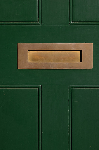 Closeup of an old wooden front door, with brass mail slot.