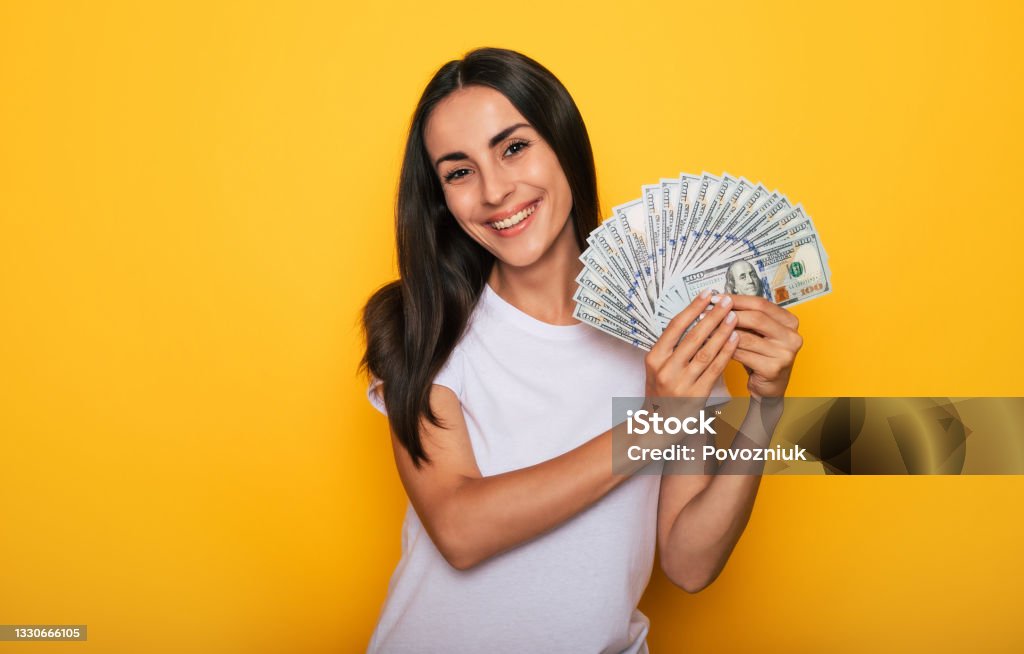 Young happy excited beautiful woman emotionally looking in the camera with a lot of money in her hands and having fun isolated on yellow background Currency Stock Photo