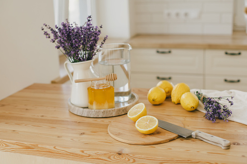 Fresh lemons, jar with honey and bunch of lavender flowers in a vase standing on a kitchen table at home. Ingridients for making lemonade. Healthy food.