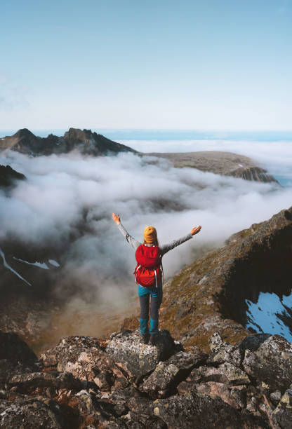 Tourist woman raised hands on mountain top over clouds travel activity summer vacations hike with backpack healthy lifestyle outdoor adventure trekking in Norway Tourist woman raised hands on mountain top over clouds travel activity summer vacations hike with backpack healthy lifestyle outdoor adventure trekking in Norway senja island photos stock pictures, royalty-free photos & images