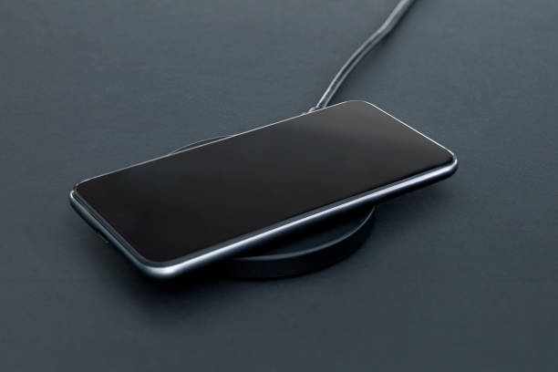 istock Close-up of luxury smartphone while recharging battery using wireless charger. Matt grey desk surface in background. 1330667972