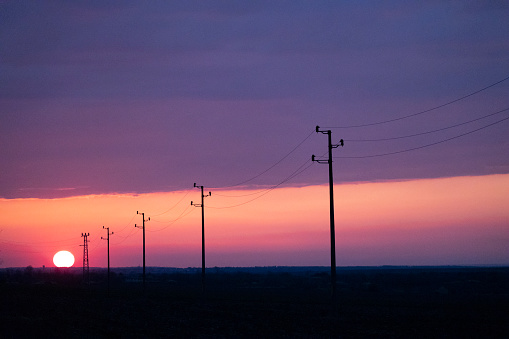 Sunset with clouds in the sky and silhouettes of electrical pylons on the road.