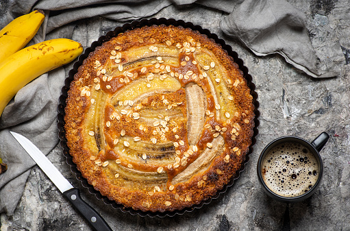 Butter free and sugar free banana bread made with oat flour,soft curd cheese and honey. Top view of full banana bread on craft plate over gray background. Ideas and recipes for healthy diet breakfast