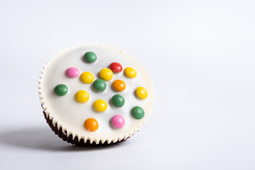 Cacao sweet homemade muffins with white chocolate and colorful bonbons on white background