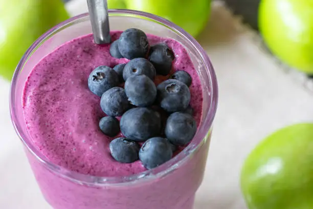 fresh blendet shake or smoothie with blueberries and green apples served in a drinking glass. Closeup view from above