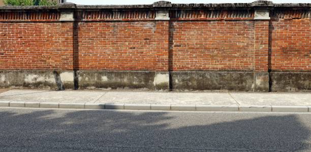 istock Old surrounding brick wall with a large concrete sidewalk and an asphalt road in front. 1330673233