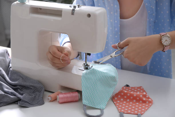 istock Woman making cloth mask with sewing machine at white table, closeup 1330675770