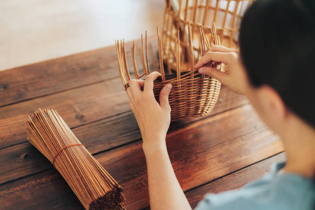 女性は木製のテーブルの上に紙管のバスケットを織ります - wicker ストックフォトと画像