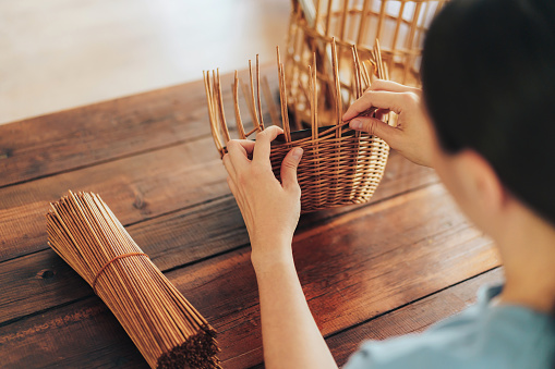 Woman weaves basket of paper tubes on wooden table.