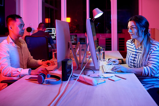 Team of software developers working on big project late at night in neon light trying to finish before deadline