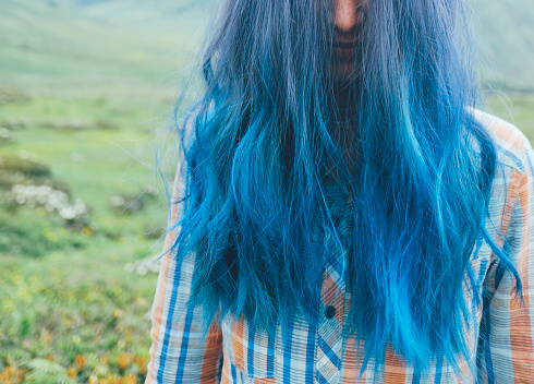 Close-up portrait of woman with blue hair. Mountain meadows in the background.