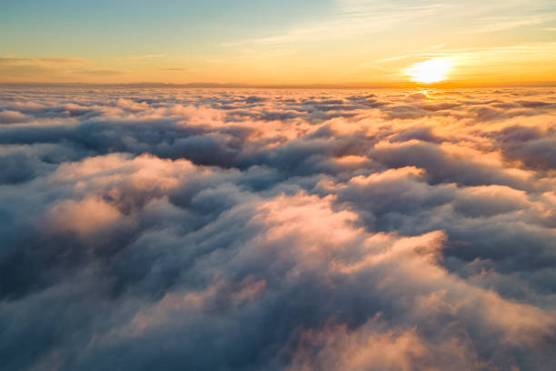 Aerial view of bright yellow sunset over white dense clouds with blue sky overhead. Aerial view of bright yellow sunset over white dense clouds with blue sky overhead. stratosphere airplane cloudscape mountain stock pictures, royalty-free photos & images