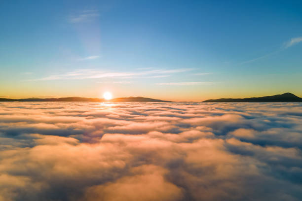 istock Aerial view of vibrant sunset over white dense clouds with distant dark mountains on horizon. 1330680251