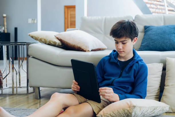 The boy using tablet computer while sitting on sofa at home. stock photo