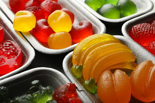 Different delicious gummy candies in containers, closeup