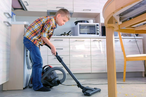 Boy is vacuuming the kitchen floor. He tidies up the corn flakes scattered on the gray tile. Side view. Boy vacuuming the kitchen floor. He tidies up the corn flakes scattered on the gray tile. Side view tidy room stock pictures, royalty-free photos & images