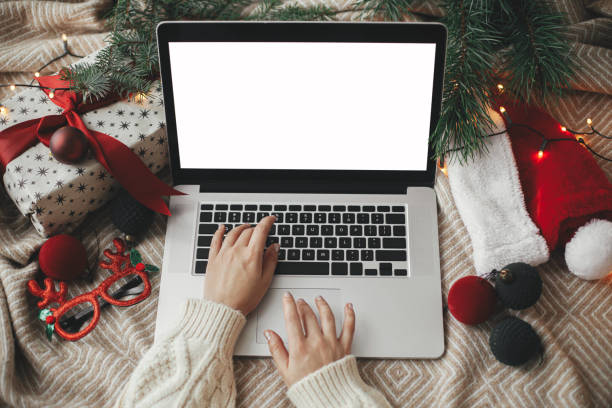 istock Hands working on laptop with blank screen on cozy bed with stylish christmas ornaments, present and santa hat. Freelance and remote work in holidays. Space for text. Shopping online. Top view 1330689642