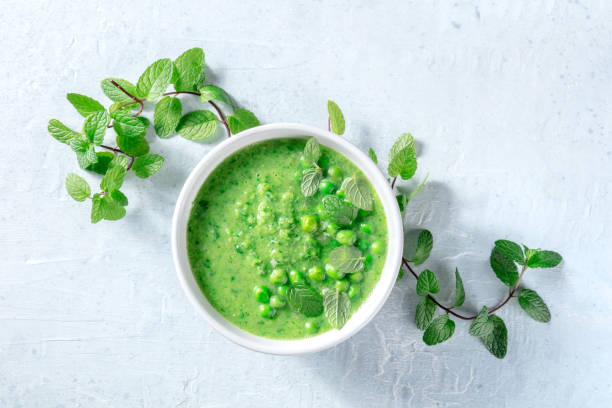 веганский суп с зеленым горошком и свежими листьями мяты, выстрел над головой - vegan pea soup стоковые фото и изображения