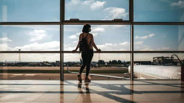 jeune femme regardant l’aéroport par la fenêtre. voyage et concept de pandémie de coronavirus - arrival airport airport lounge flying photos et images de collection