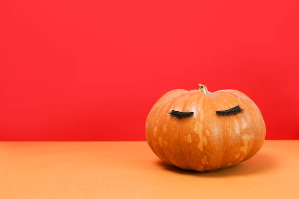 istock Halloween pumpkin with false eyelashes on red. Minimal Holiday season concept background. 1330694531