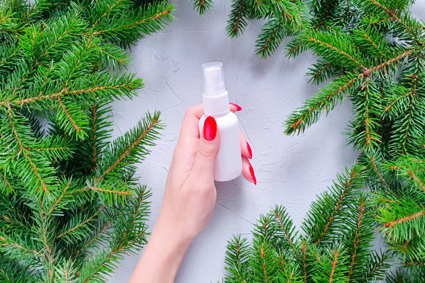 istock Unbranded white plastic spray bottle, female hand with red nails and fir tree on gray table. Natural organic spa cosmetics concept and liquid antibacterial spray. Mockup. 1330697347
