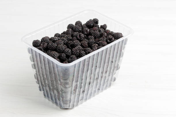 istock Fresh black raspberries in a plastic box on white wooden table. 1330697478