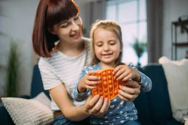 Photo of pretty mother sitting on sofa at home and playing pop pit game with her cheerful little daughter