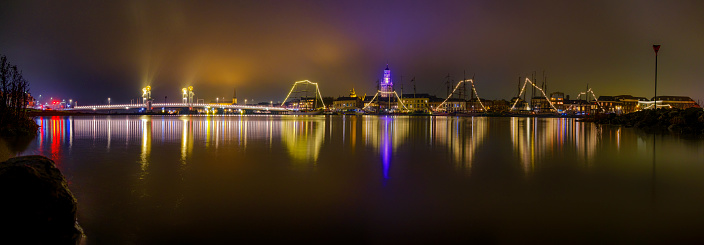 Evening on the skyline of the city of Kampen in Overijssel, The Netherlands. The lights of the city are reflected in the calm water while the sky has turned blue right after sunset.