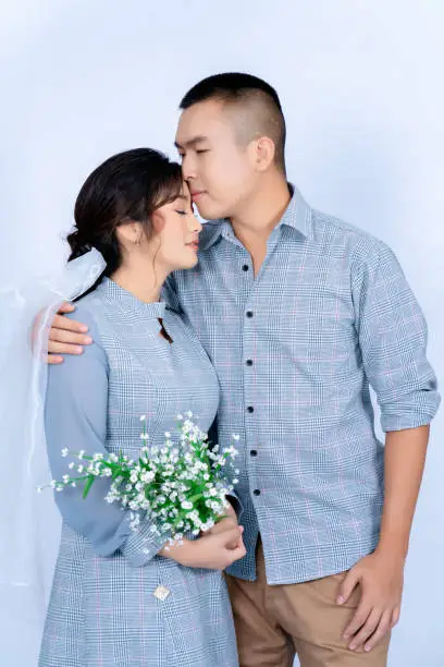 Pre-wedding portrait of a young Asian couple dressed in the same blue tones, happily posing for each other's expressions of love against a white background.