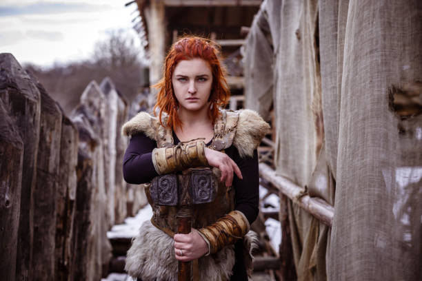 Viking woman with hammer in a traditional warrior clothes. Viking woman with hammer in a traditional warrior clothes. Against the backdrop of a large viking village. palisade boundary stock pictures, royalty-free photos & images